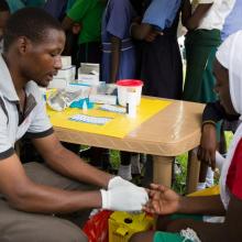  A young man testing a girl for HIV by pricking her finger and drawing blood.